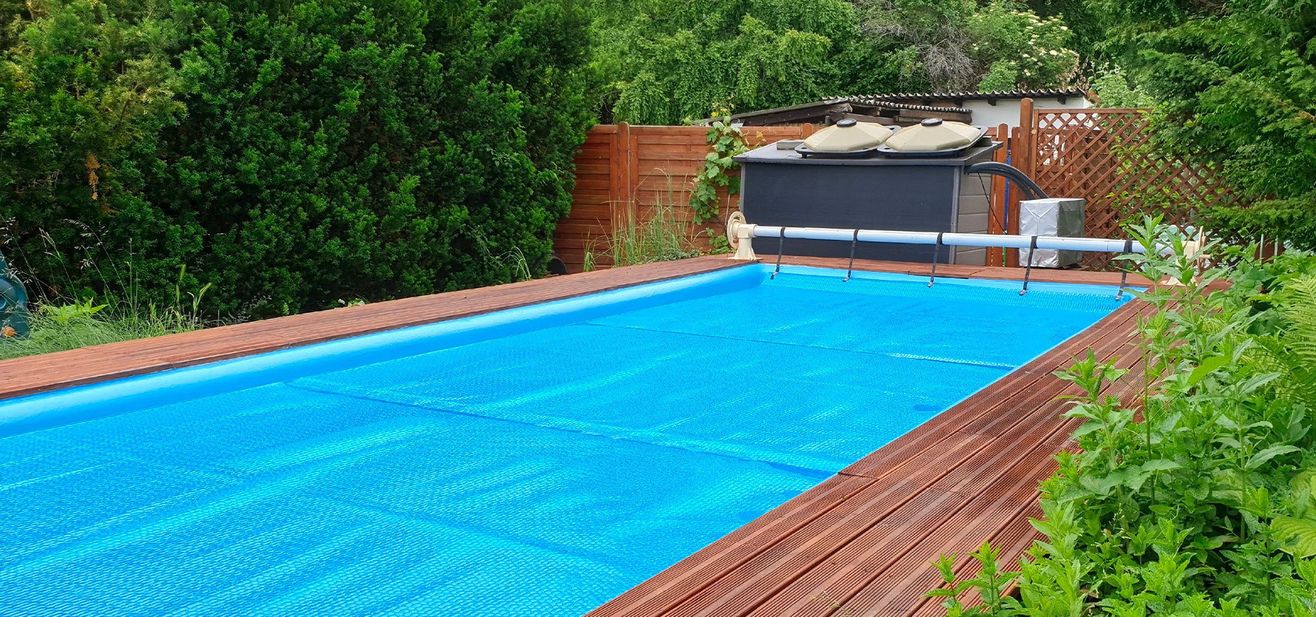 Description pour la balise alt SEO : "Piscine extérieure avec couverture bleue, entourée par un deck en bois et une végétation dense, dans un jardin arrière privé."